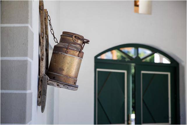 Rustikale Dekoration mit alter Milchkanne an der Hauswand und traditioneller Holztür im Hintergrund.