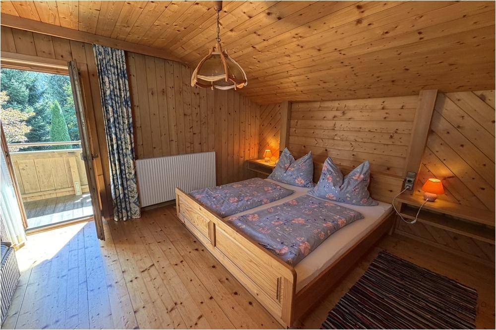 Gemütliches Schlafzimmer mit Holzvertäfelung, Doppelbett und Zugang zum Balkon mit Bergblick.