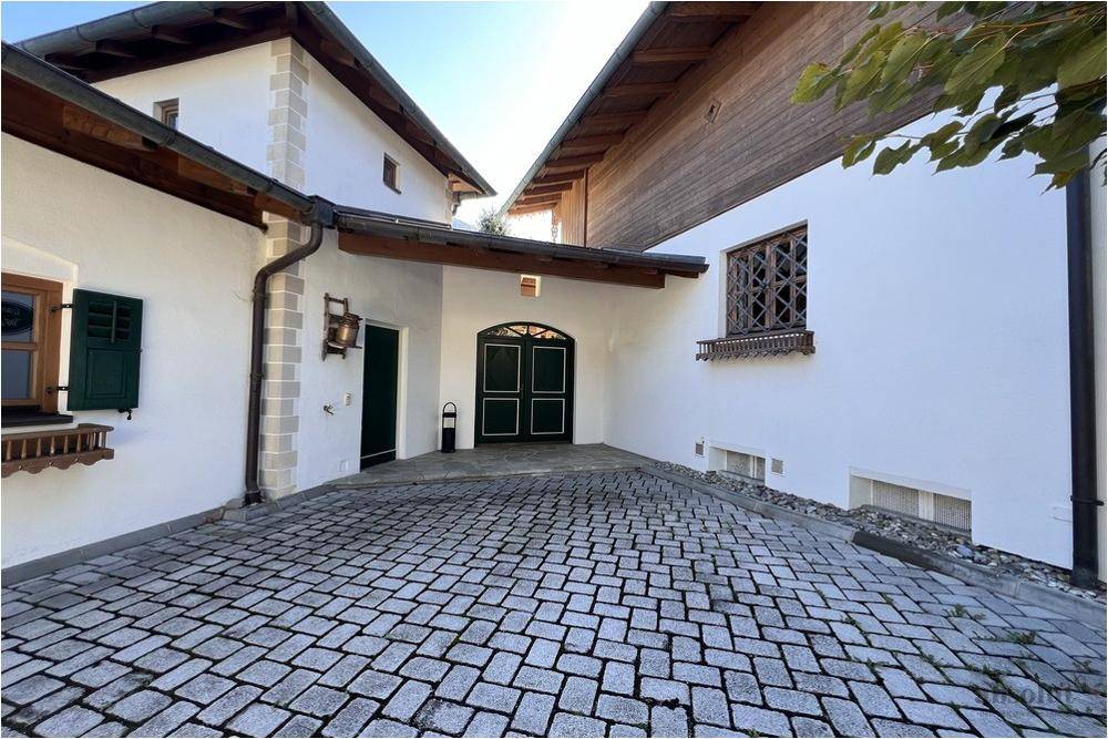 Eingangsbereich des Hauses mit gepflastertem Hof, Holztüren und traditionellen Fensterläden.