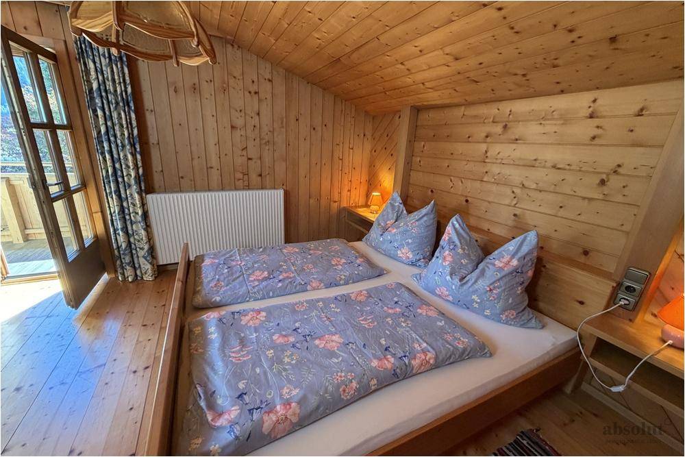 Helles Schlafzimmer im Dachgeschoss mit Holzverkleidung, Doppelbett und direktem Balkonzugang.