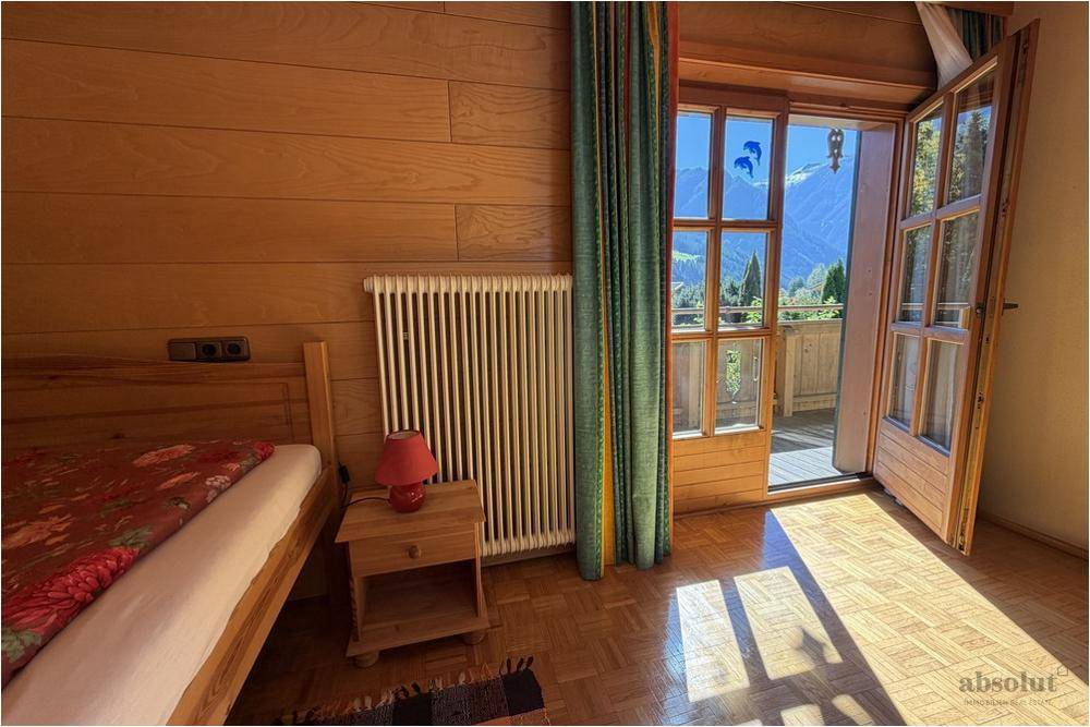 Helles Schlafzimmer mit Holzwänden, Einzelbett und direktem Zugang zum Balkon mit Panoramablick.