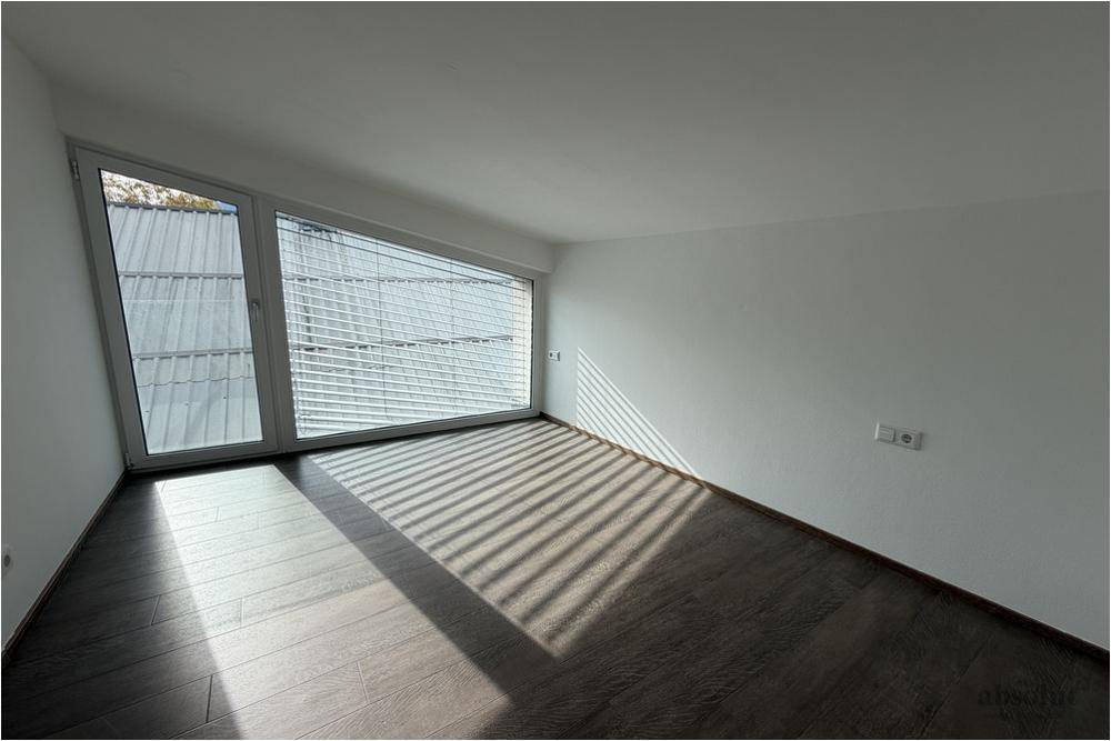 Sonniger Raum mit Laminatboden und großen Fenstern, die den Raum erhellen.