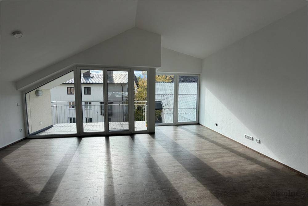 Geräumiger Wohnbereich mit großen Fenstern, Laminatboden und Zugang zu einem Balkon.
