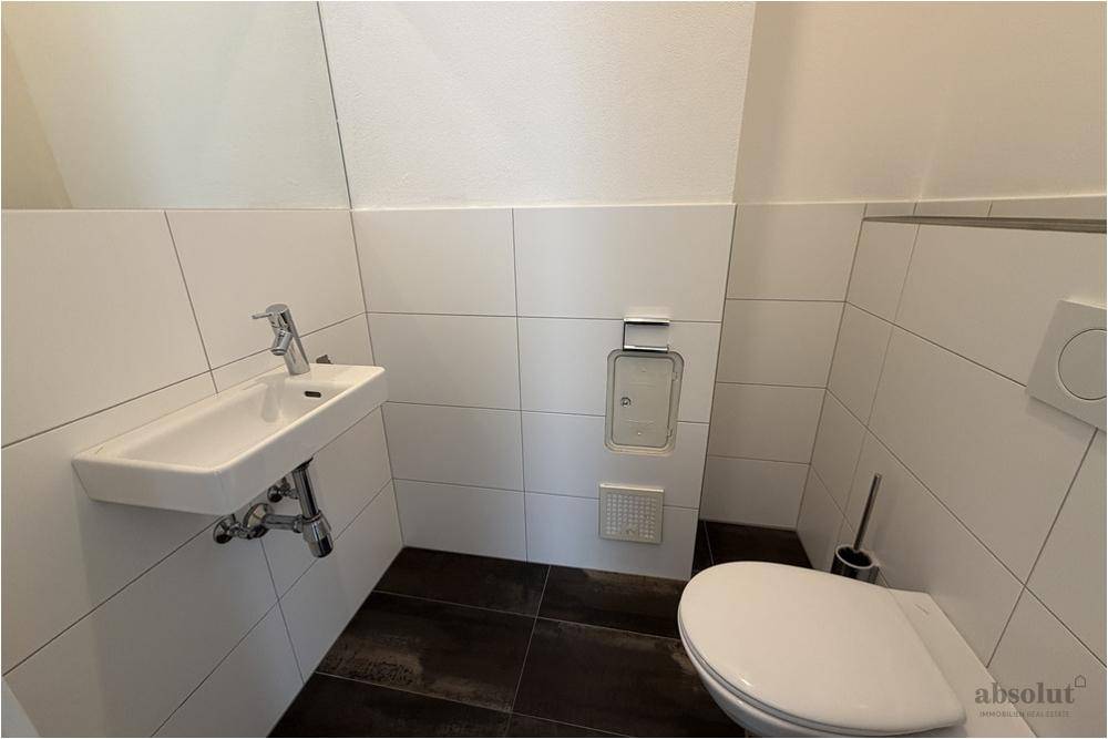 Kleines Gäste-WC mit Wand-WC, Waschbecken und weißen Fliesen.