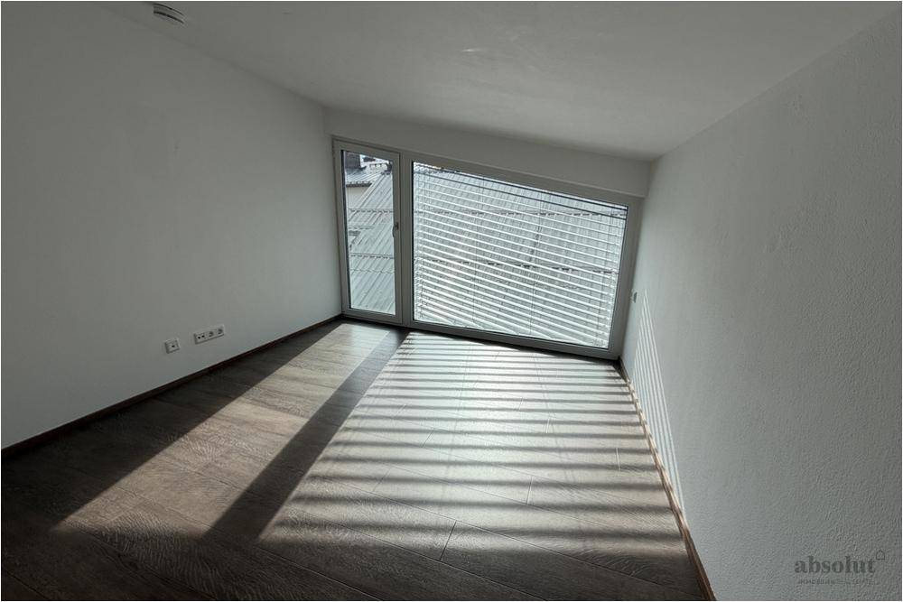Lichtdurchflutetes Zimmer mit Laminatboden und breiten Fenstern mit Jalousien.
