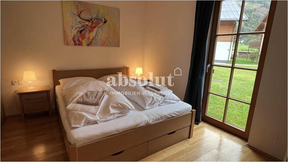 Schlafzimmer mit Holzbett und großen Fenstern, die direkten Zugang zum Garten bieten.