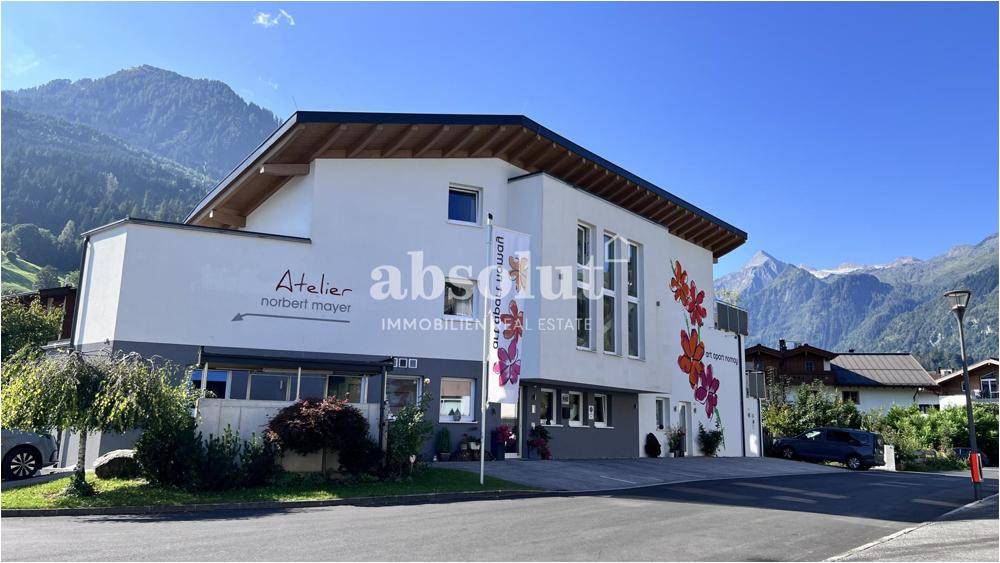 Modernes Gebäude mit weißer Fassade und künstlerischer Blumenmalerei vor alpiner Kulisse.