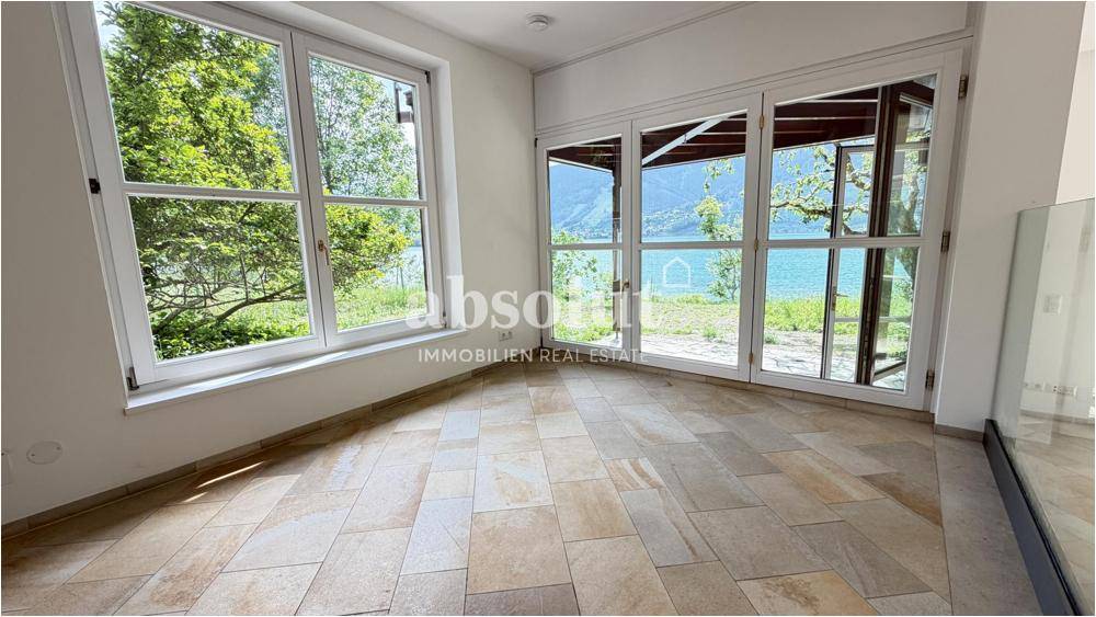 Heller Raum mit großen Fenstern, die einen weiten Blick auf den See und die Berge bieten.