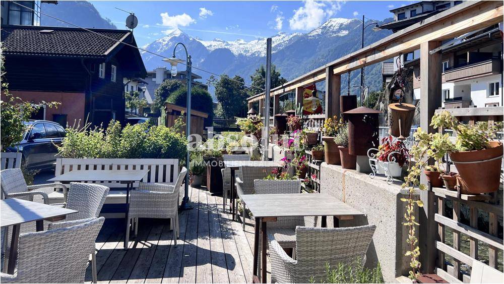 Geräumige Außenterrasse mit Bergblick, ausgestattet mit Tischen und Korbstühlen unter blauem Himmel.