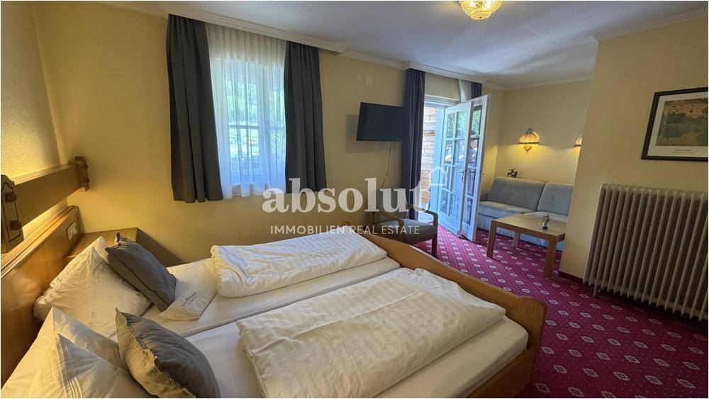 Geräumiges Schlafzimmer mit zwei Betten, Sofa und Balkonzugang, traditionell eingerichtet.