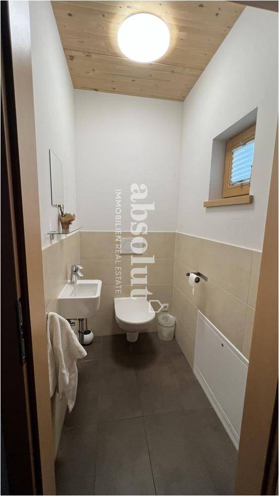 Kleines Gäste-WC mit Fenster, Waschbecken und Wand-WC, teilweise gefliest.
