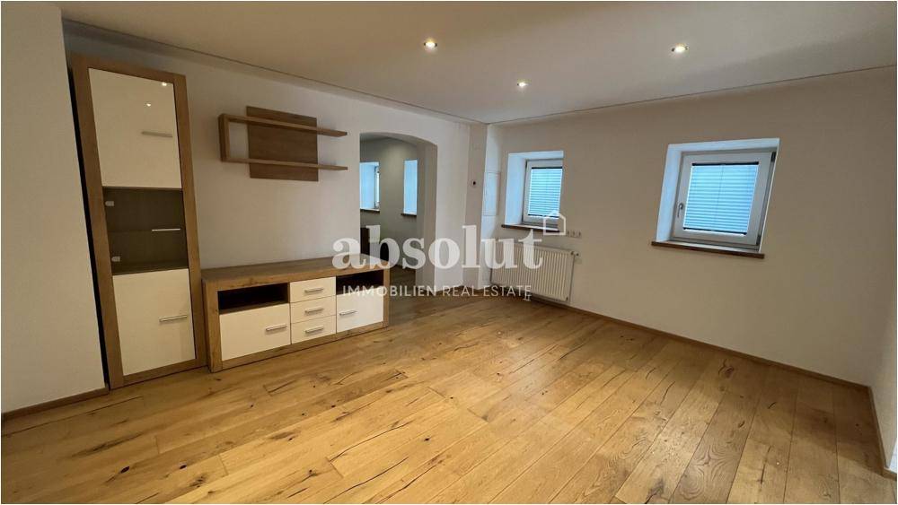 Geräumiges Wohnzimmer mit Holzboden, zwei Fenstern und moderner Einrichtung.
