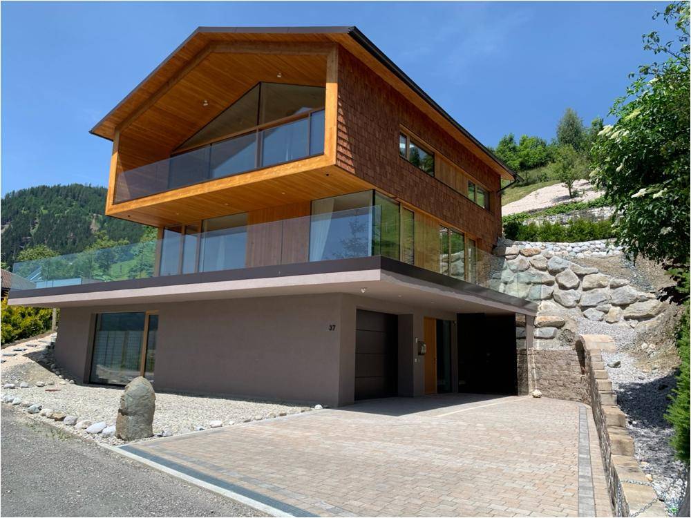 Modernes Holzhaus mit großen Glasfronten, Balkonen und integrierter Garage in alpiner Umgebung.