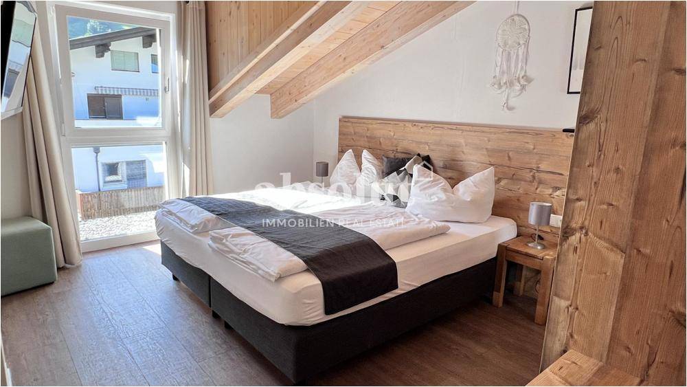 Helles Schlafzimmer mit Holzbalkendecke, großem Bett und Blick auf die grüne Umgebung.