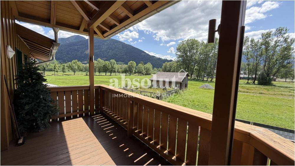 Heller Holzbalkon mit weitem Blick über grüne Felder und Berge.