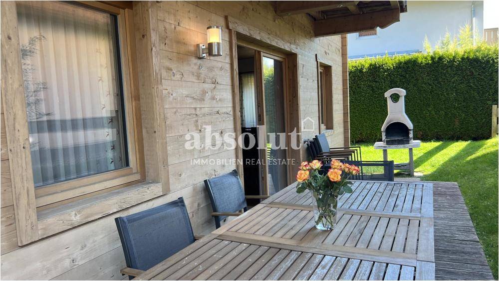 Sonniger Terrassenbereich mit Holztisch, Grill und Rasenfläche, ideal für Mahlzeiten im Freien.