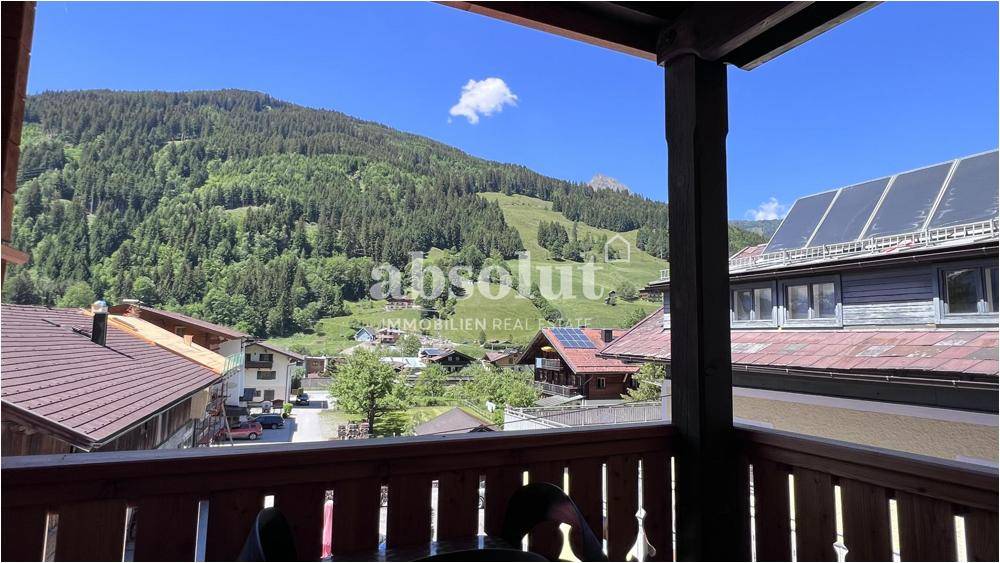 Panoramablick von einem Holzbalkon auf die umliegende Berglandschaft und das Dorf.