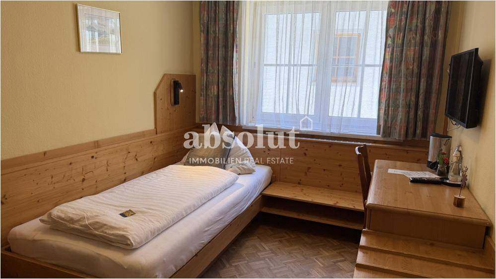 Einzelzimmer mit Holzvertäfelung, Einzelbett und Schreibtisch, hell durch großes Fenster.