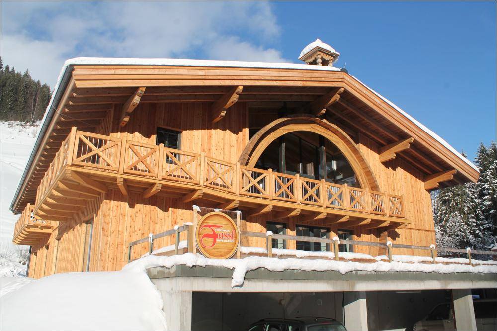 Holzchalet im Winter mit Schnee bedeckt, umgeben von verschneiten Bergen und Wäldern.