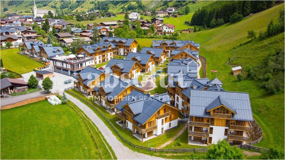 Luftaufnahme einer Wohnanlage im Chalet-Stil, eingebettet in eine grüne Berglandschaft.