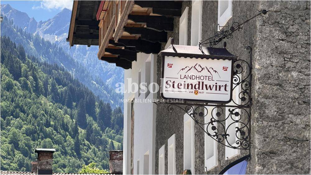 Traditionelles Hotelschild vor einer beeindruckenden Bergkulisse mit grünen Wäldern.