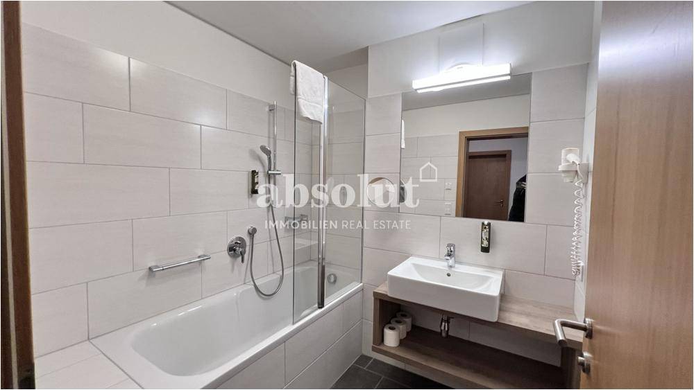 Modernes Badezimmer mit Badewanne inklusive Duschfunktion, Waschbecken und hellen Fliesen.