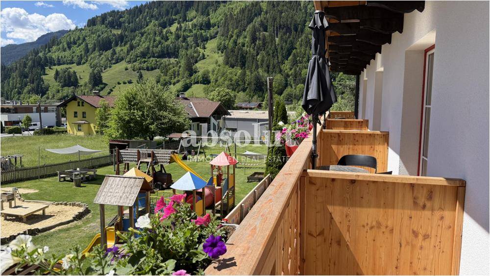 Balkon mit Blumenkästen und Blick auf einen Kinderspielplatz und die grüne Umgebung.