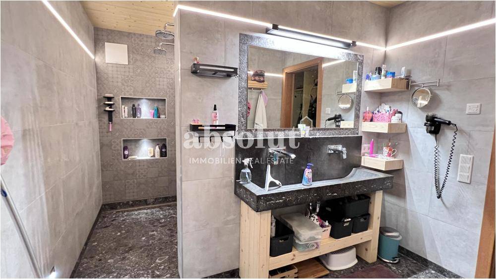 Modernes Badezimmer mit begehbarer Dusche, Steinwaschbecken und indirekter Beleuchtung.