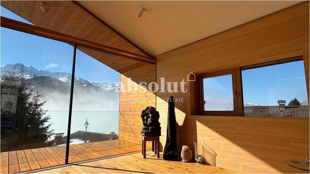 Helles Wohnzimmer mit Holzwänden, großen Glasfronten und weitem Blick auf die Bergwelt.