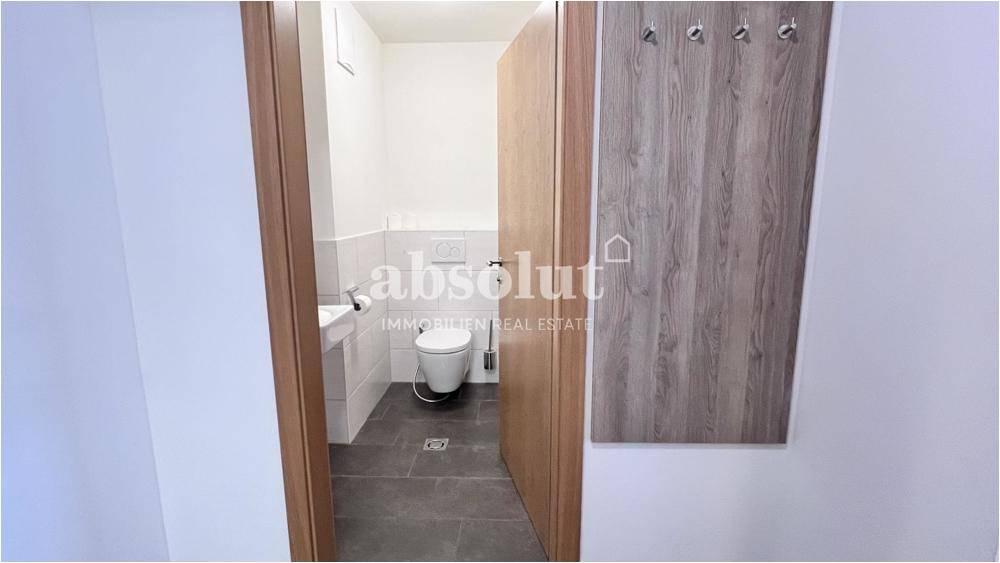 Separates Gäste-WC mit Wand-WC, kleinem Waschbecken und dunklen Bodenfliesen.