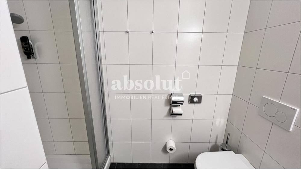 Modernes Badezimmer mit weißen Fliesen, Duschkabine und wandhängendem WC für Komfort und Hygiene.