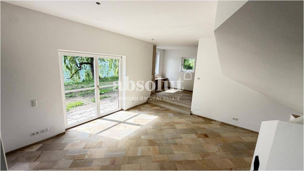 Geräumiges Wohnzimmer mit großen Fenstern, Seeblick und hellem Fliesenboden, unmöbliert.