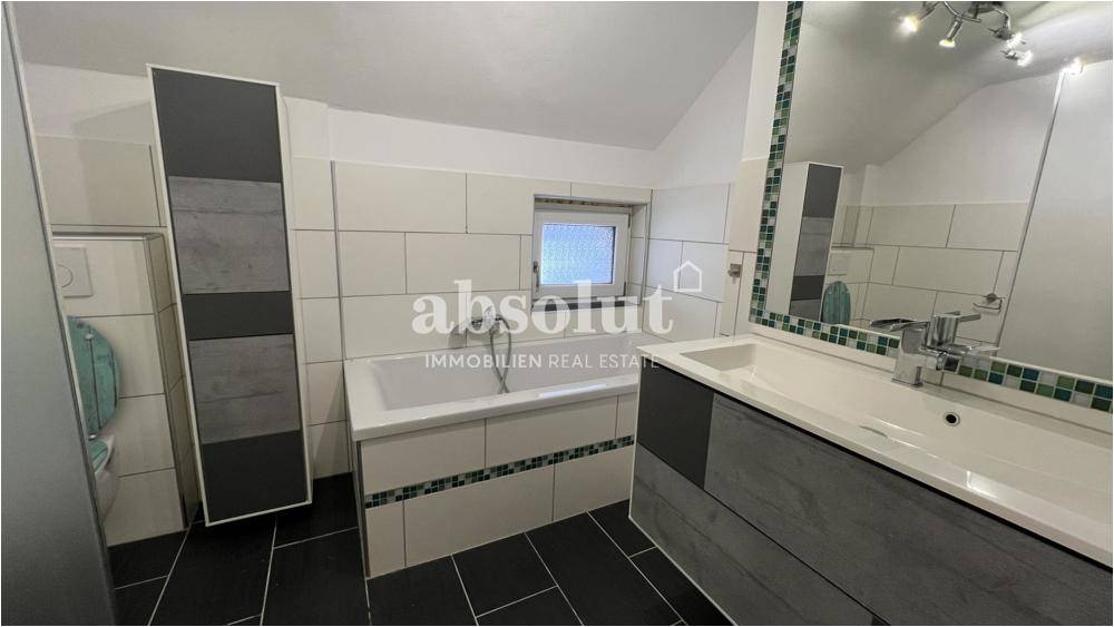 Modernes Badezimmer mit Badewanne, Waschbecken und dunklen Fliesen.