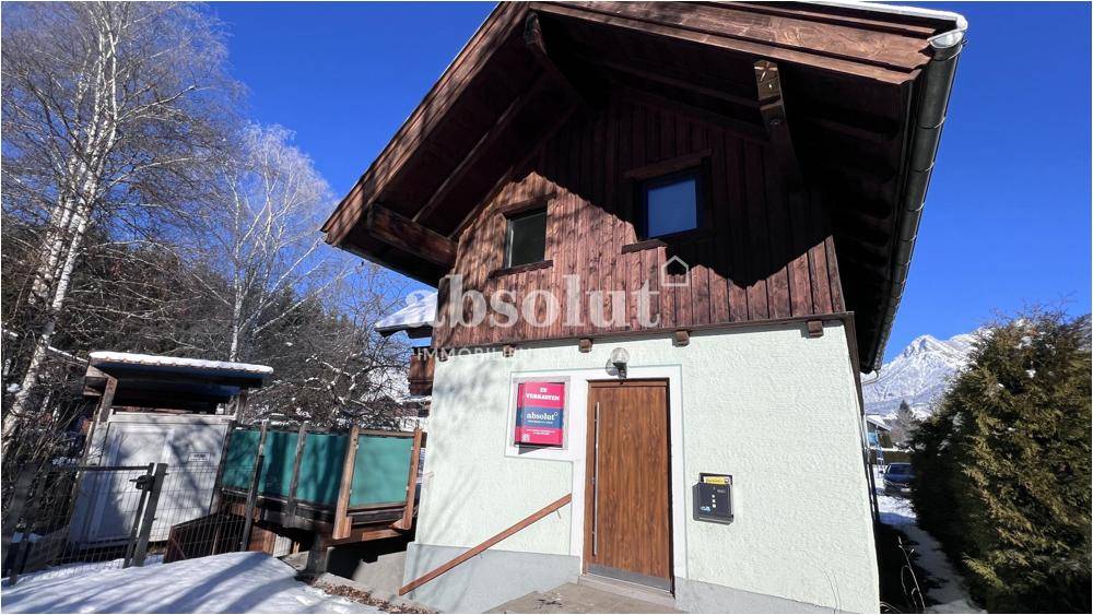 Charmante Chalet-Fassade mit Holzverkleidung und Putz, umgeben von Schnee und mit Bergblick.