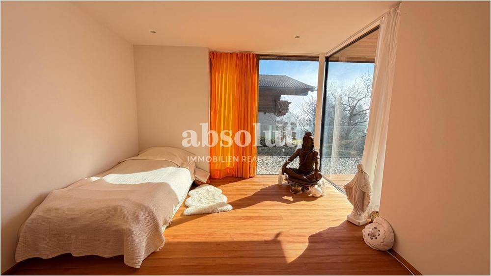 Helles Schlafzimmer mit Holzboden, großen Fenstern und Blick auf die umliegende Landschaft.