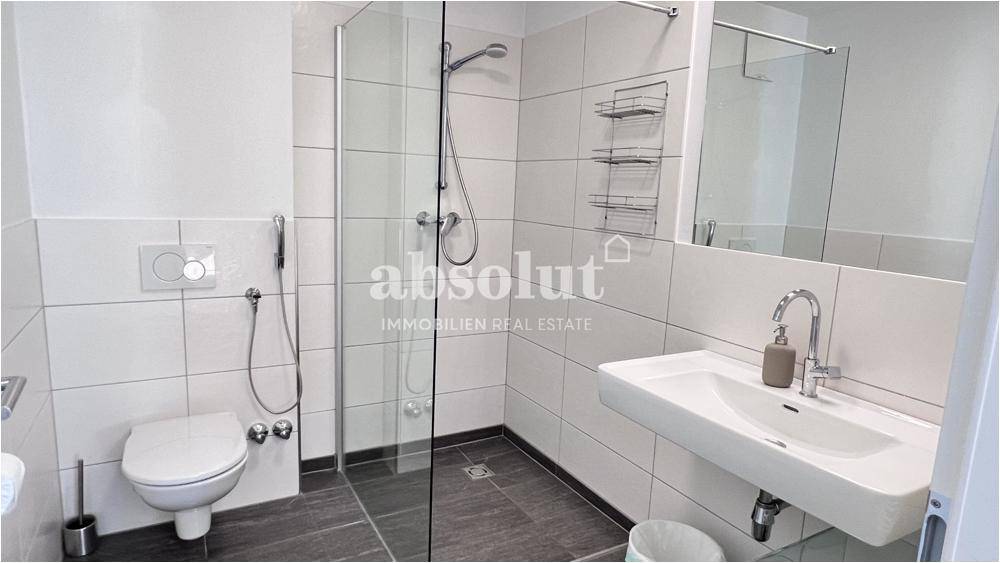 Modernes Badezimmer mit Duschkabine, Wand-WC und Waschtisch in hellen Fliesen.