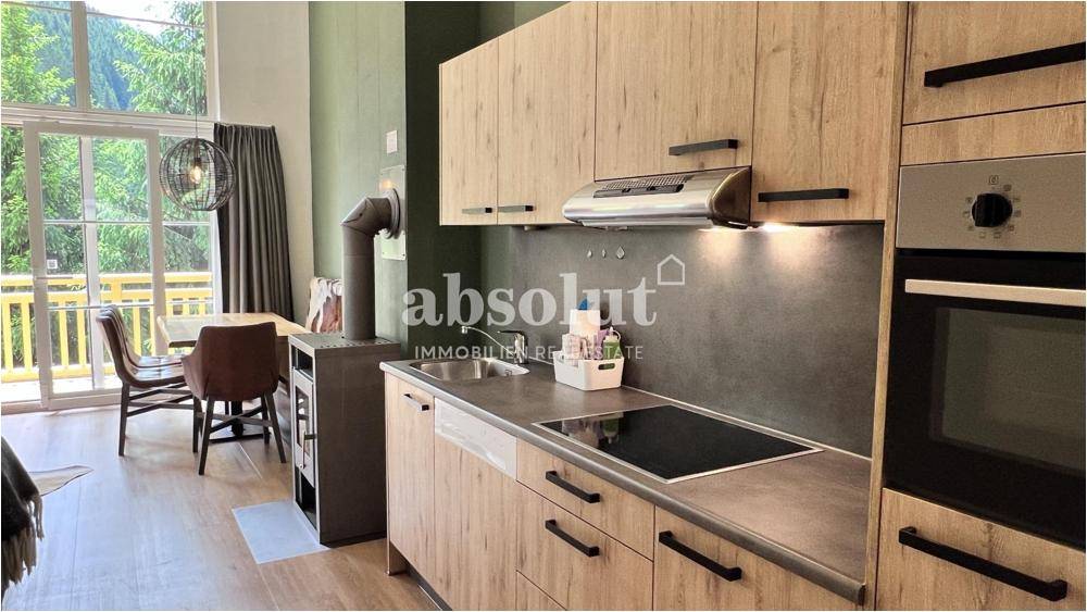 Offener Wohnbereich mit integrierter Küche, Kaminofen und Zugang zum Balkon.