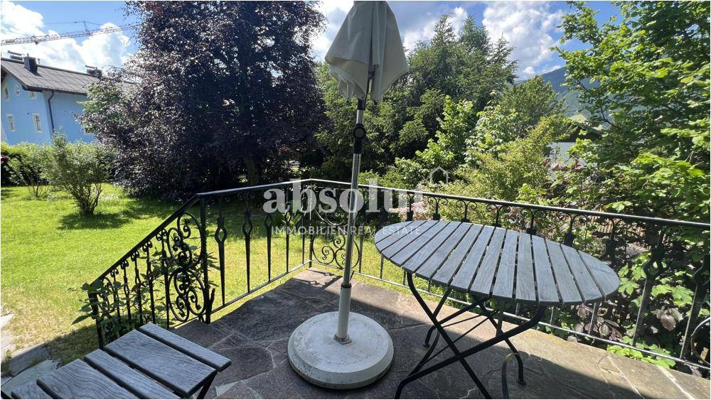 Kleine Terrasse mit Sitzgelegenheiten und Sonnenschirm, umgeben von viel Grün.
