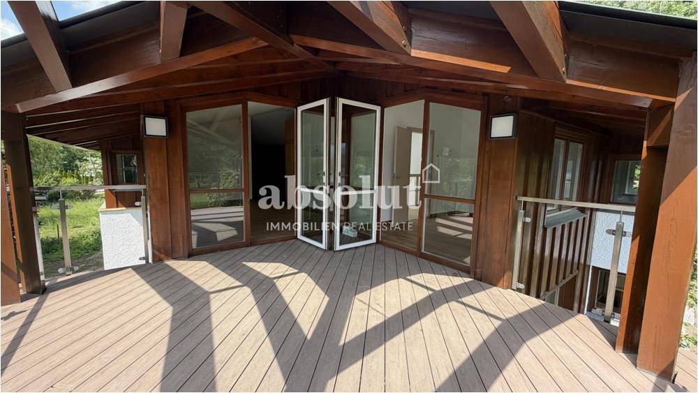 Überdachte Terrasse mit Holzboden und Zugang zu Innenräumen, mit weitem Seeblick.