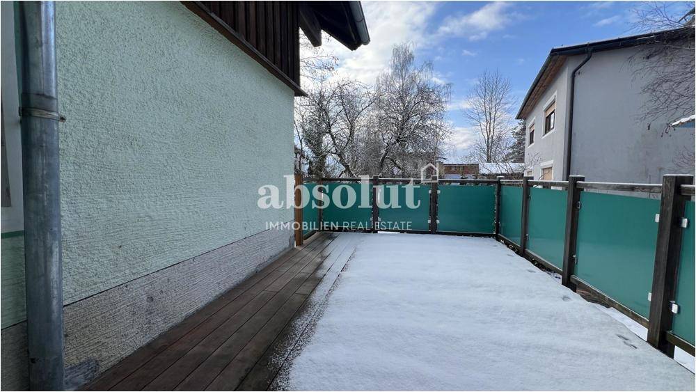Außenterrasse mit Holzboden und grüner Sichtschutzwand, bedeckt mit Schnee.