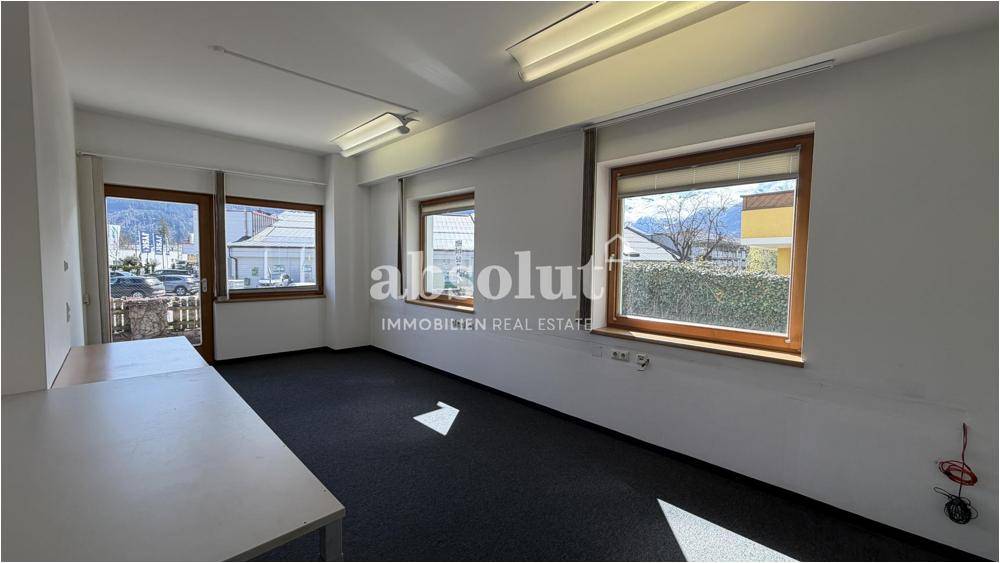 Geräumiges Büro mit dunklem Teppichboden, viel Tageslicht und Blick ins Grüne.