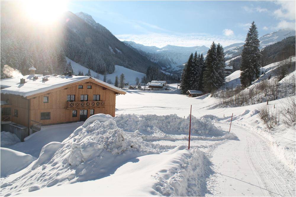 Idyllisches Holzchalet in einer verschneiten Berglandschaft unter strahlend blauem Himmel.