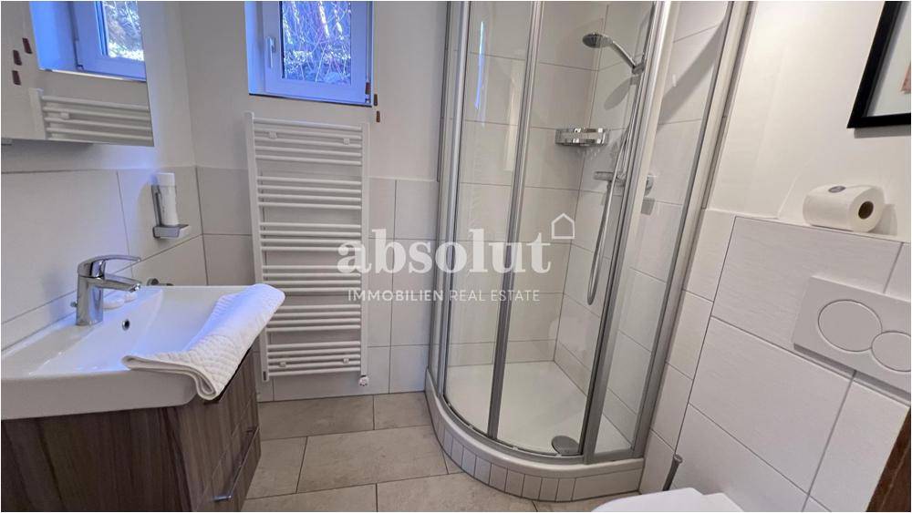 Modernes Badezimmer mit Dusche, Waschbecken und beheiztem Handtuchhalter, hell gefliest.