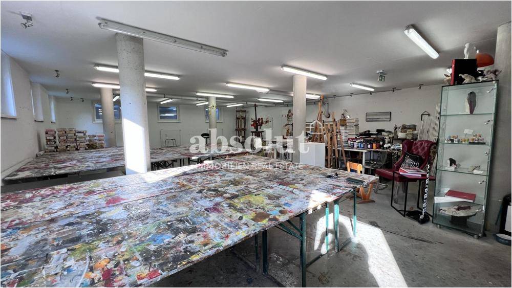 Weitläufiger Werkstattraum mit langen Tischen, Kunstmaterialien und viel Tageslicht.