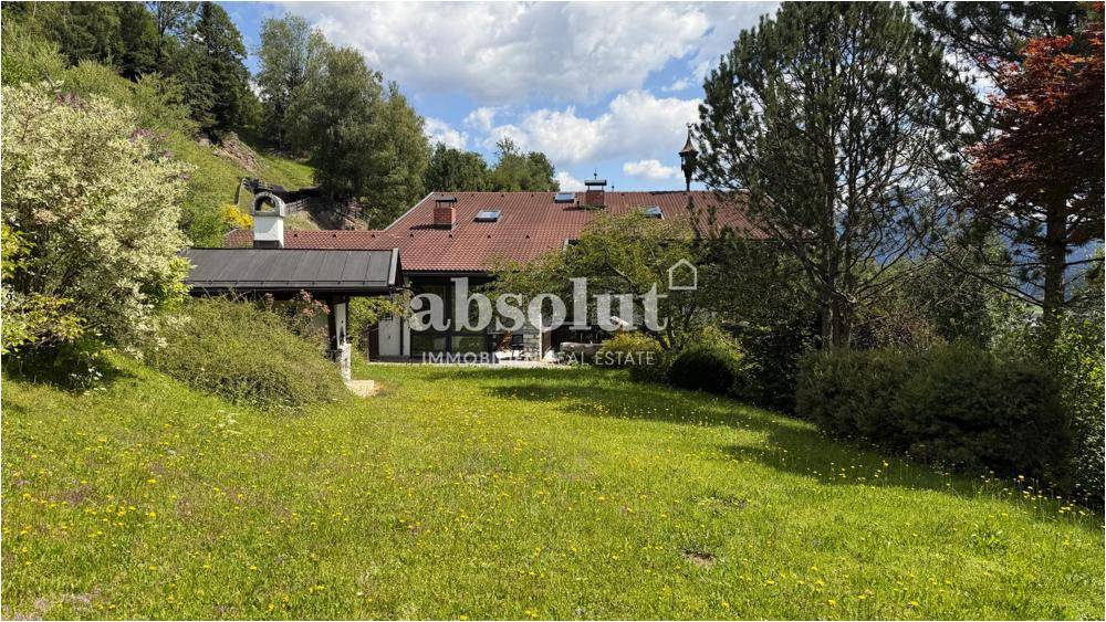 Das Haus vom weitläufigen Garten aus gesehen, umgeben von grünen Wiesen und hohen Bäumen.