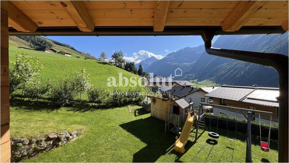 Überdachter Balkon mit Blick auf den Garten, Spielplatz und die umliegende Berglandschaft.