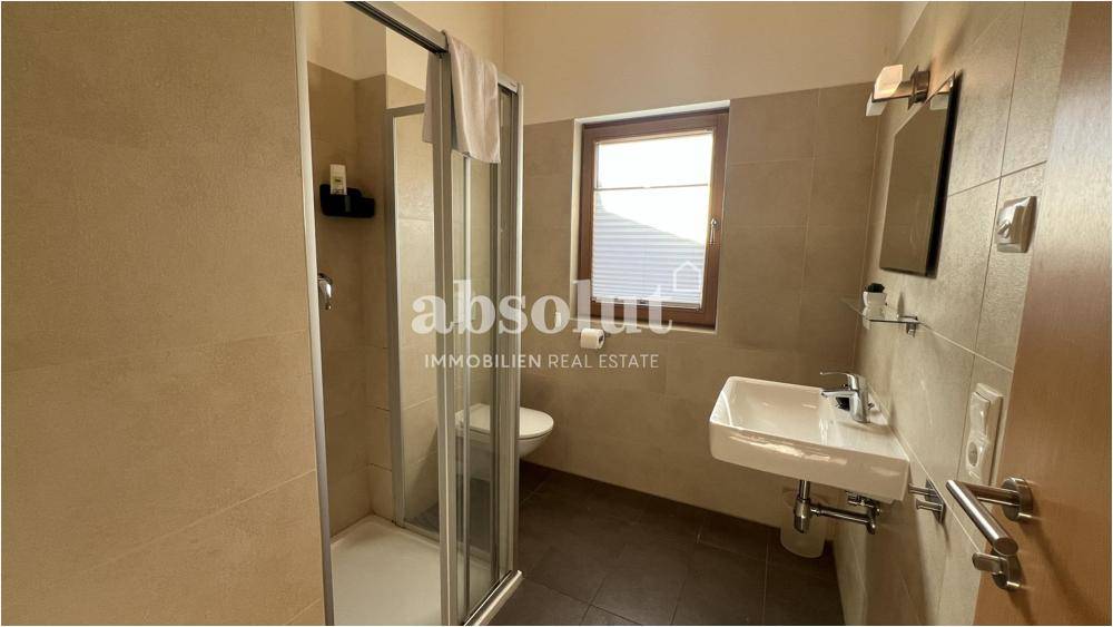 Modernes Badezimmer mit Duschkabine, Waschbecken und Fenster, hell gefliest.