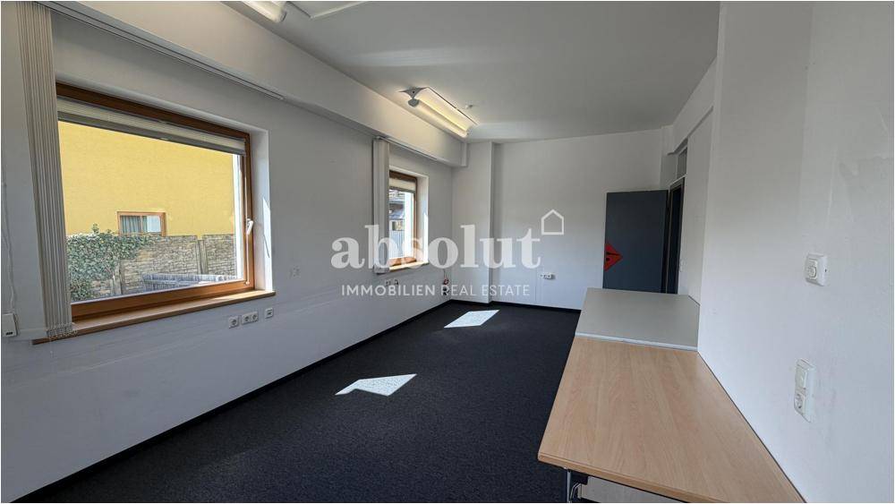 Funktionales Büro mit Schreibtisch, Teppichboden und Fenstern mit Blick auf die Umgebung.