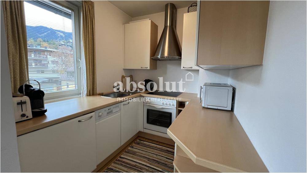 Funktionale Küchenzeile mit hellen Schränken, Holz-Arbeitsplatte und Fenster mit Bergblick.