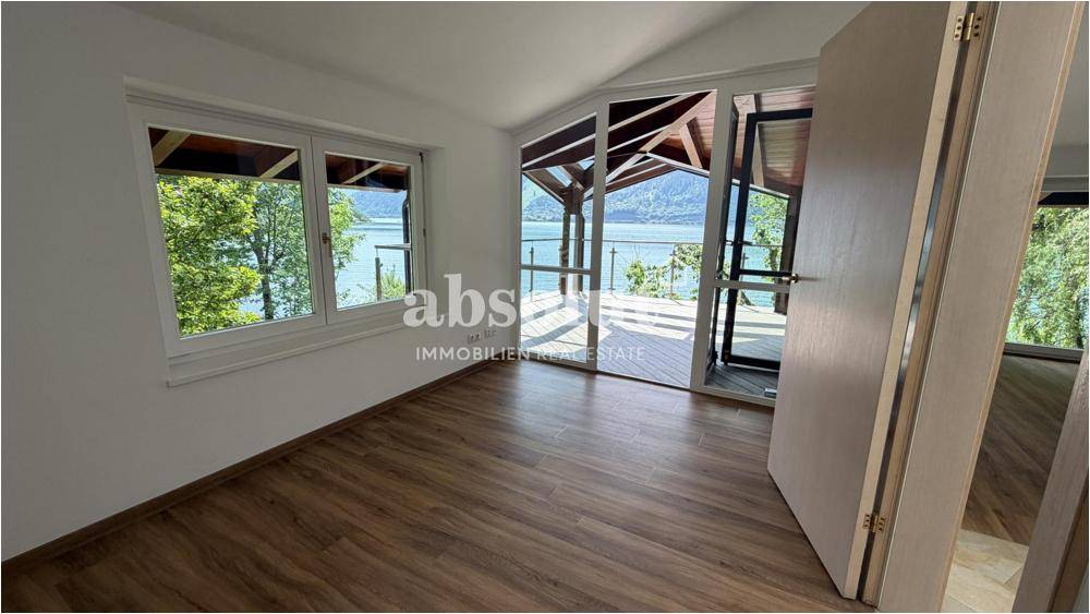 Schlafzimmer mit Seeblick, Holzboden und Zugang zu einer überdachten Terrasse, unmöbliert.